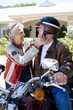 Photo: Senior man sitting on motorbike on driveway, senior woman adjusting strap of man’s crash helmet, smiling, side view Senior man sitting on motorbike on driveway, senior woman adjusting strap of man’s crash helmet, smiling, side view