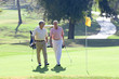 Photo: Two mature men playing golf, walking side by side on putting green, holding golf clubs, smiling Two mature men playing golf, walking side by side on putting green, holding golf clubs, smiling