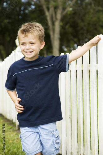 Photo: little boy standing by picket fence little boy standing by picket fence