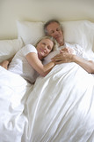 Photo: Mature couple lying in bed, man sleeping, woman leaning contentedly on man’s chest, smiling, portrait Mature couple lying in bed, man sleeping, woman leaning contentedly on man’s chest, smiling, portrait