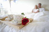 Photo: Mature couple sitting upright in bed, focus on breakfast tray with two coffee cups and single red rose in foreground Mature couple sitting upright in bed, focus on breakfast tray with two coffee cups and single red rose in foreground