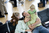Photo: Family waiting in airport departure lounge, boy (8-10) and girl (7-9) watching parents sleeping, smiling, elevated view Family waiting in airport departure lounge, boy (8-10) and girl (7-9) watching parents sleeping, smiling, elevated view