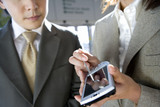 Photo: Businessman and woman standing in airport, looking at businesswoman’s personal electronic organiser, close-up, mid-section Businessman and woman standing in airport, looking at businesswoman’s personal electronic organiser, close-up, mid-section