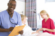 Photo: Female nurse by mature female patient in hospital bed, male nurse in smiling foreground Female nurse by mature female patient in hospital bed, male nurse in smiling foreground