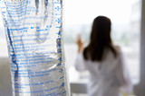 Photo: IV bag, young female doctor looking out window in background (differential focus) IV bag, young female doctor looking out window in background (differential focus)
