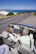 Photo: South Africa, Cape Town, senior couple parked on side of road by sea in convertible silver car, looking at map, elevated view South Africa, Cape Town, senior couple parked on side of road by sea in convertible silver car, looking at map, elevated view