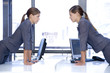 Identical female twins looking at each other over an office desk with computers