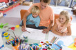 Photo: Father sitting with son and daughter(6-8) art and crafts table, smiling, elevated view Father sitting with son and daughter(6-8) art and crafts table, smiling, elevated view
