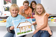 Photo: Boy and girl (6-8) holding up painting of house, parents in background, smiling, portrait Boy and girl (6-8) holding up painting of house, parents in background, smiling, portrait
