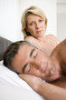 Couple on bed, man asleep in foreground, portrait of woman in background