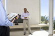 Photo: Man standing in living room of house, smiling, male real estate agent in foreground Man standing in living room of house, smiling, male real estate agent in foreground