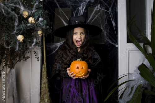 Photo: Girl in a witch's costume at a Hallowe'en party, holding a pumpkin Girl in a witch's costume at a Hallowe'en party, holding a pumpkin
