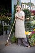 Woman florist standing at the entrance to her shop, leaning on a broom