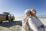 Photo: Senior woman embracing senior man from behind on beach by camper van, smiling, portrait Senior woman embracing senior man from behind on beach by camper van, smiling, portrait
