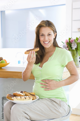 Photo: Young pregnant woman with plate of pastries holding donut, smiling, portrait Young pregnant woman with plate of pastries holding donut, smiling, portrait
