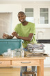 Photo: Young man putting empty glass jar and can into recycling bin in kitchen, smiling, portrait Young man putting empty glass jar and can into recycling bin in kitchen, smiling, portrait