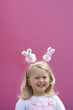 Girl (2-4) wearing bunny rabbit headband by pink wall, smiling, portrait