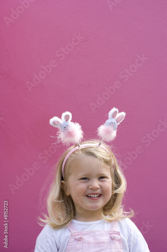 Photo: Girl (2-4) wearing bunny rabbit headband by pink wall, smiling, portrait Girl (2-4) wearing bunny rabbit headband by pink wall, smiling, portrait