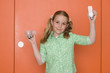 Girl (9-11) holding up light bulbs by orange door and wall, smiling, portrait