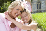 Photo: Flower girl (10-12) embracing grandmother, church in background, smiling, portrait, close-up Flower girl (10-12) embracing grandmother, church in background, smiling, portrait, close-up