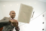 Photo: Businessman by pen and paperwork on glass table, smiling, low angle view through glass Businessman by pen and paperwork on glass table, smiling, low angle view through glass