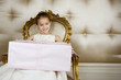 Photo: Little girl sitting in an ornate chair wearing a party dress holding a large present Little girl sitting in an ornate chair wearing a party dress holding a large present