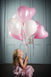 little girl sitting on the floor looking up at her bunch of balloons