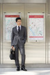 Photo: Businessman with briefcase and newspaper listening to MP3 player, by maps on wall Businessman with briefcase and newspaper listening to MP3 player, by maps on wall