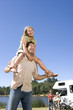 Foto: Girl (9-11) on father's shoulders, mother and brother (10-12) by motor home in background, low angle view Girl (9-11) on father's shoulders, mother and brother (10-12) by motor home in background, low angle view