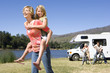 Girl (9-11) on mother's back, father and brother (10-12) by motor home in background