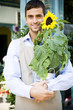 Male florist standing outside his shop, holding a potted sunflower