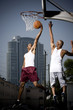 Foto: Two Young African American man jumping with a basketball on an urban basketball court Two Young African American man jumping with a basketball on an urban basketball court