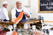 Fishmonger behind counter holding up fillet of fish, smiling, portrait