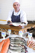 Fishmonger behind counter in shop, holding fish, portrait