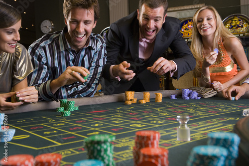 Men and women gambling at roulette table in casino, smiling