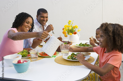Photo: Family of four at dinner table, mother pouring water for daughter (7-9) Family of four at dinner table, mother pouring water for daughter (7-9)