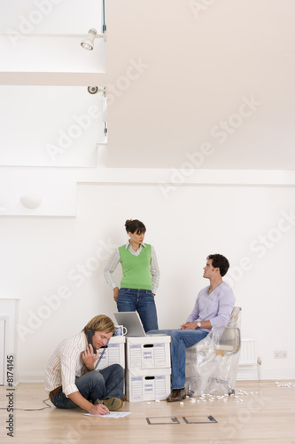 Photo: Man on telephone by colleagues at laptop computer by boxes Man on telephone by colleagues at laptop computer by boxes
