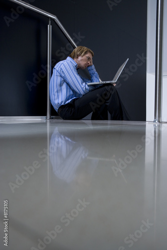 Photo: Businessman with laptop computer on stairs, low angle view Businessman with laptop computer on stairs, low angle view