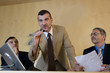 Businessman speaking into microphone, flanked by colleagues