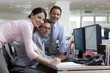 Businessman at desk flanked by colleagues, smiling, portrait