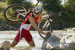 A man carrying his bike across a stream.
