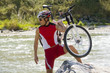 A man carrying his bike across a stream.