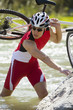 A man carrying his bike across a stream.