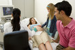 Pregnant woman having ultrasound scan, smiling at daughter (9-11) by husband