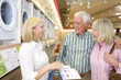 Mature couple in appliance shop smiling at shop assistant with brochure