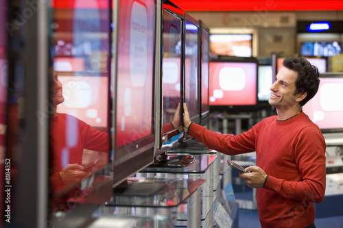 Photo: Young man shopping for television, smiling, side view Young man shopping for television, smiling, side view