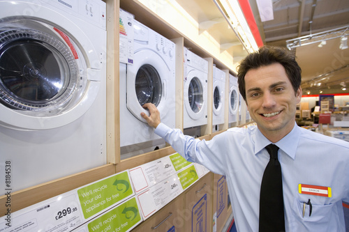 Foto: Young salesman by washing machines, smiling, portrait Young salesman by washing machines, smiling, portrait