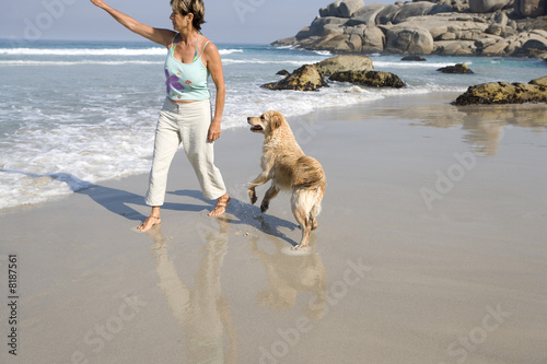 Photo: Mature woman with dog on beach, arm outstretched Mature woman with dog on beach, arm outstretched