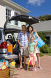 Family of three by luggage and open boot of car, smiling, portrait