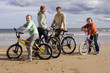 Family of four standing with bicycles on beach, smiling, portrait